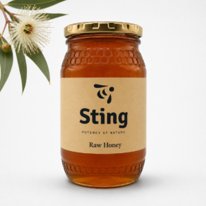 Jar of Sting Raw Honey with a gold lid and beige label, honey reaching the bottom, on a white background with a eucalyptus flower on the left.