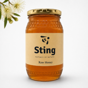 Jar of Sting Raw Honey with a gold lid and beige label, set against a white background. A small sprig of white flowers is visible on the left.